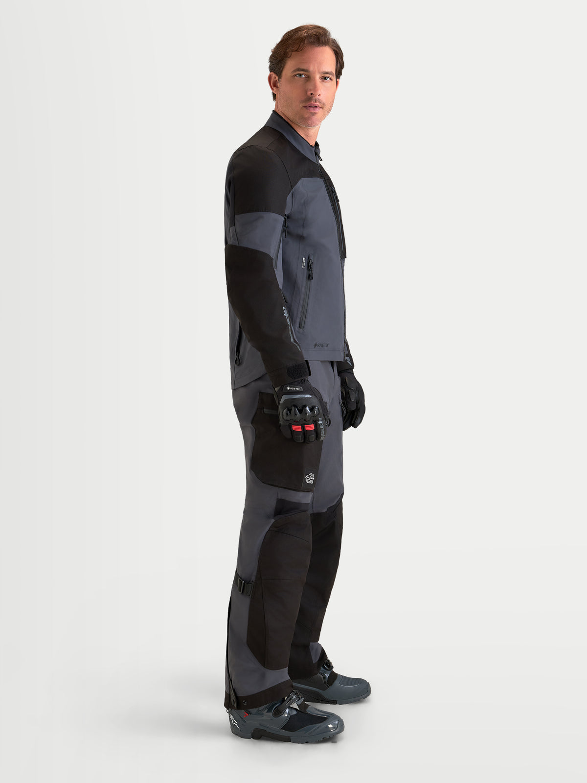 Alpinestars Arenis Gore-Tex Jacke, Herren-Adventure-Motorradjacke in Schwarz und Dunkelgrau, Seitenprofilansicht mit wasserdichter Textilkonstruktion und ergonomischem Kragen, getragen von einem Model.