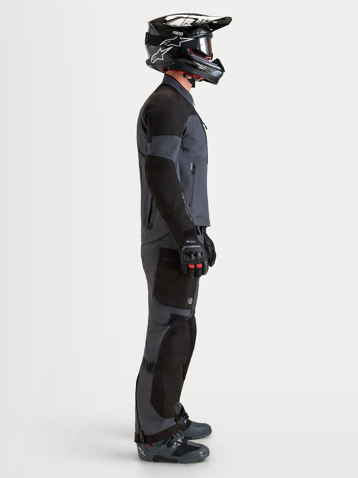 Alpinestars Arenis Gore-Tex Gear Set, Herren-Abenteuer-Motorradjacke und -hose in Schwarz und Dunkelgrau, Seitenansicht an einem Model mit passendem Helm und Stiefeln, wasserdichte All-Terrain-Schutzausrüstung