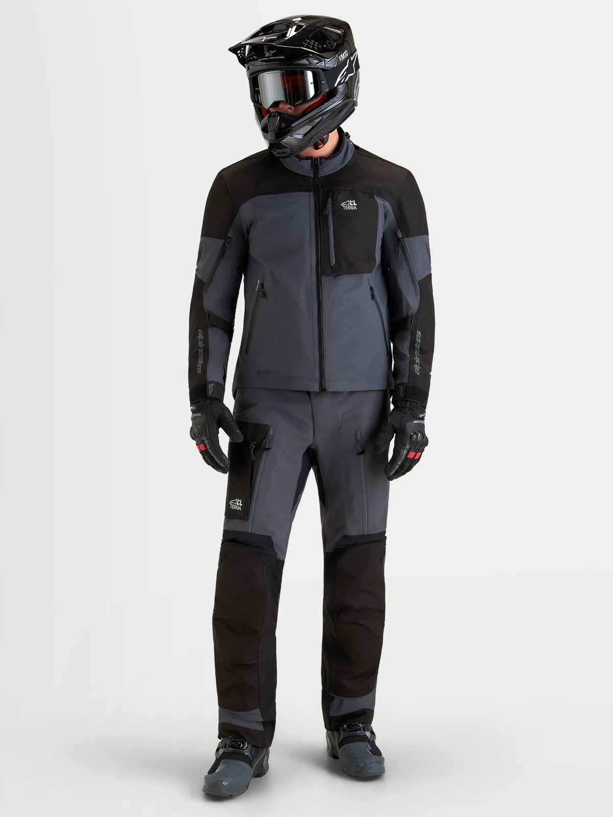 Alpinestars Arenis Gore-Tex® Gear Set, Herren-Adventure-Motorradjacke und -hose in Schwarz und Dunkelgrau, Vorderansicht des Modells mit passender Ausrüstung und Helm, wasserdichte All-Terrain-Schutzausrüstung