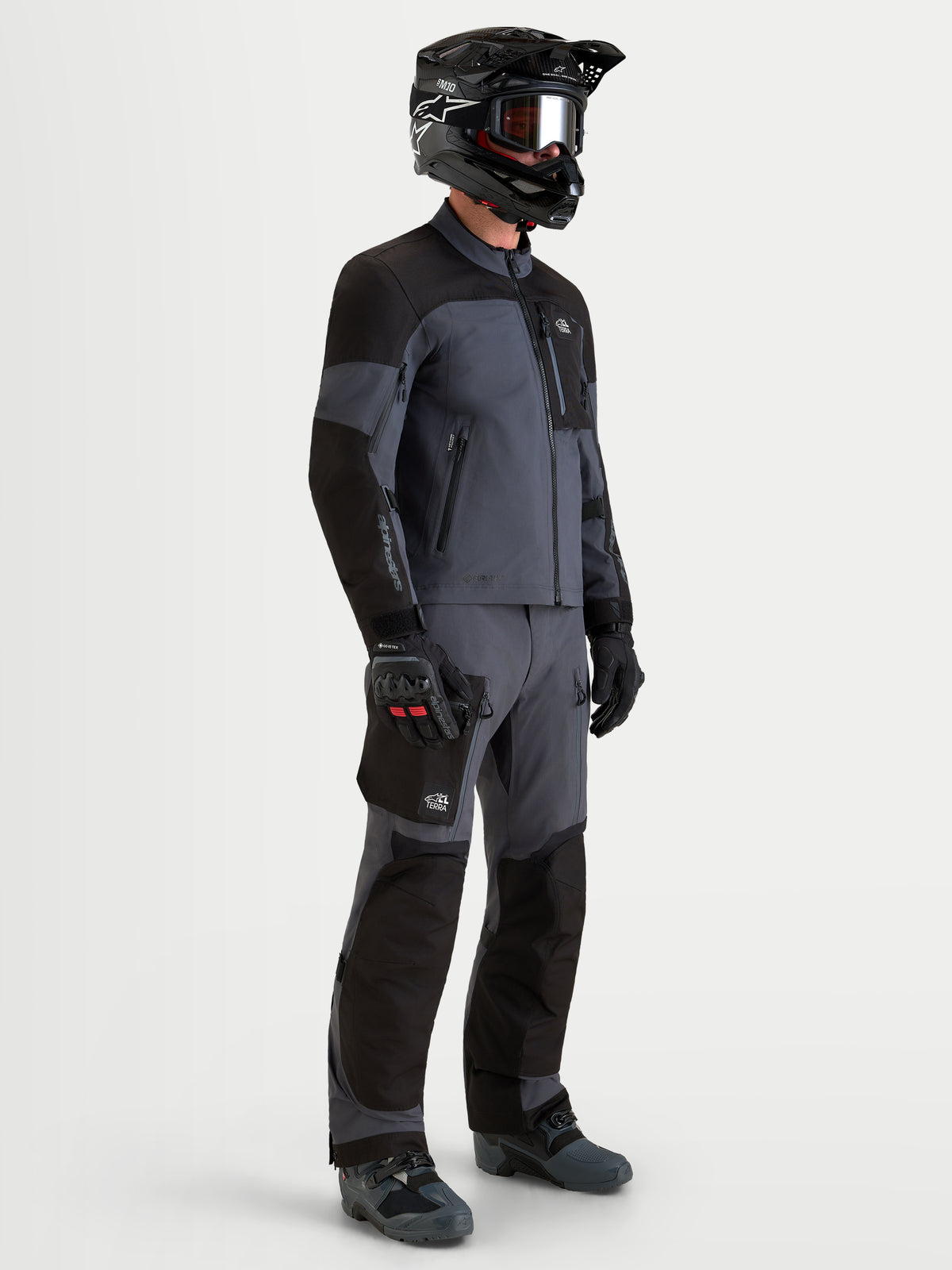 Alpinestars Arenis Gore-Tex Gear Set, Herren-Adventure-Motorradjacke und -hose in Schwarz und Dunkelgrau, Seitenprofilansicht an einem Model mit passender Ausrüstung und Helm, wasserdichte All-Terrain-Fahrbekleidung