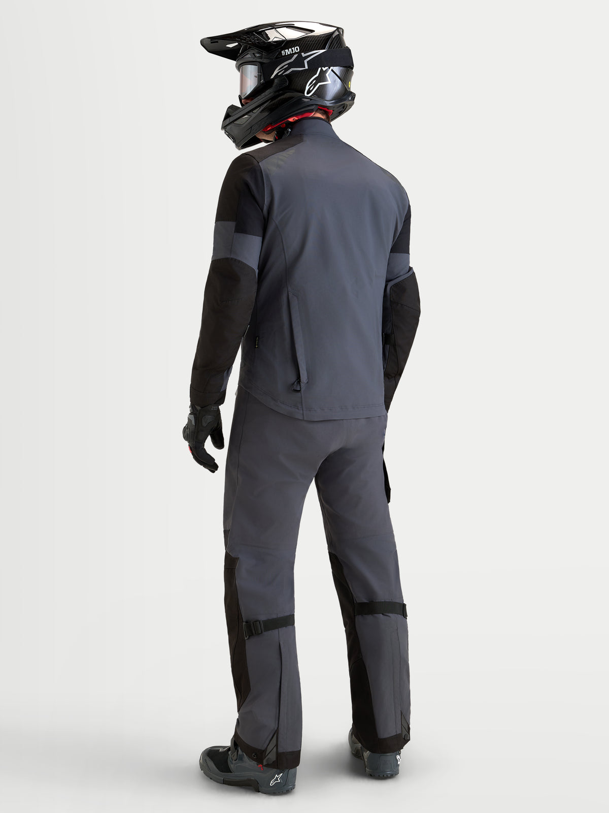 Alpinestars Arenis Gore-Tex® Gear Set, Herren-Adventure-Motorradkombi in Grau und Schwarz, Rückansicht an Model mit passendem Helm, wasserdichte All-Terrain-Schutzausrüstung