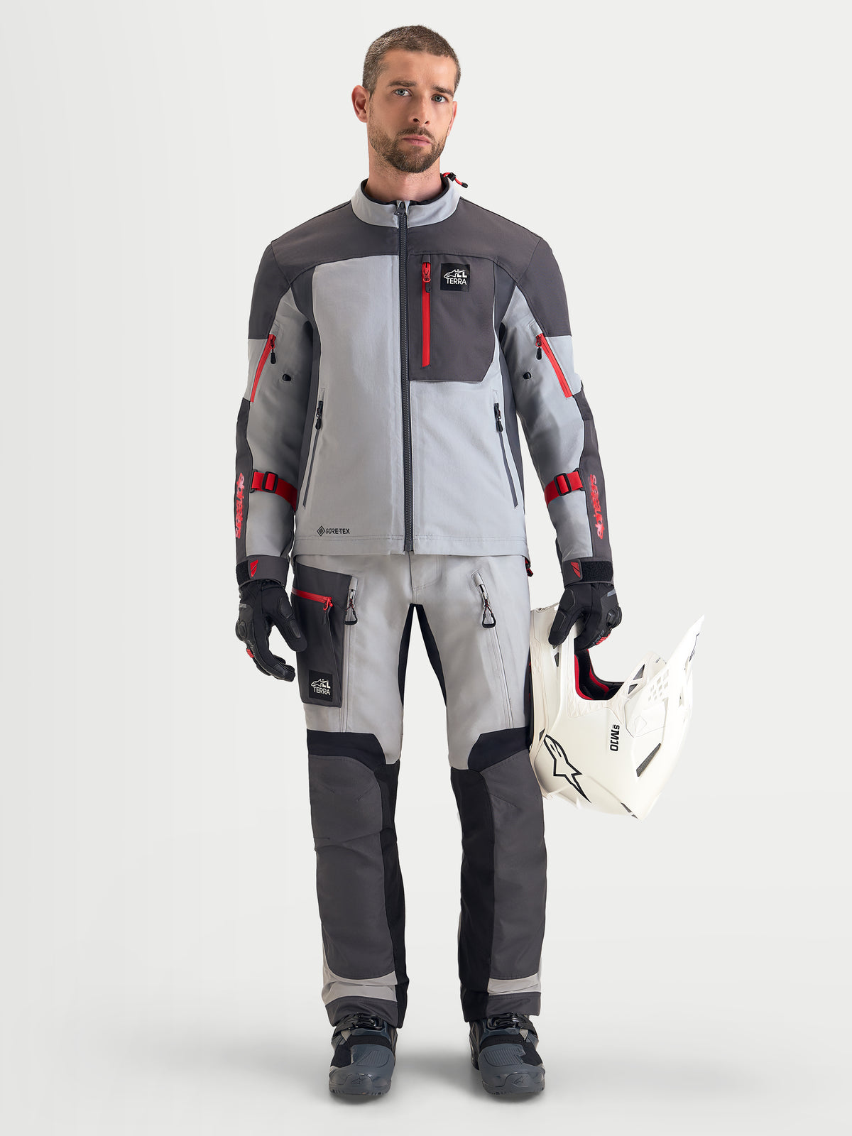 Alpinestars Arenis Gore-Tex Jacket, men's adventure touring motorcycle jacket in mid gray, deep gray, and black, worn by a model holding a white helmet