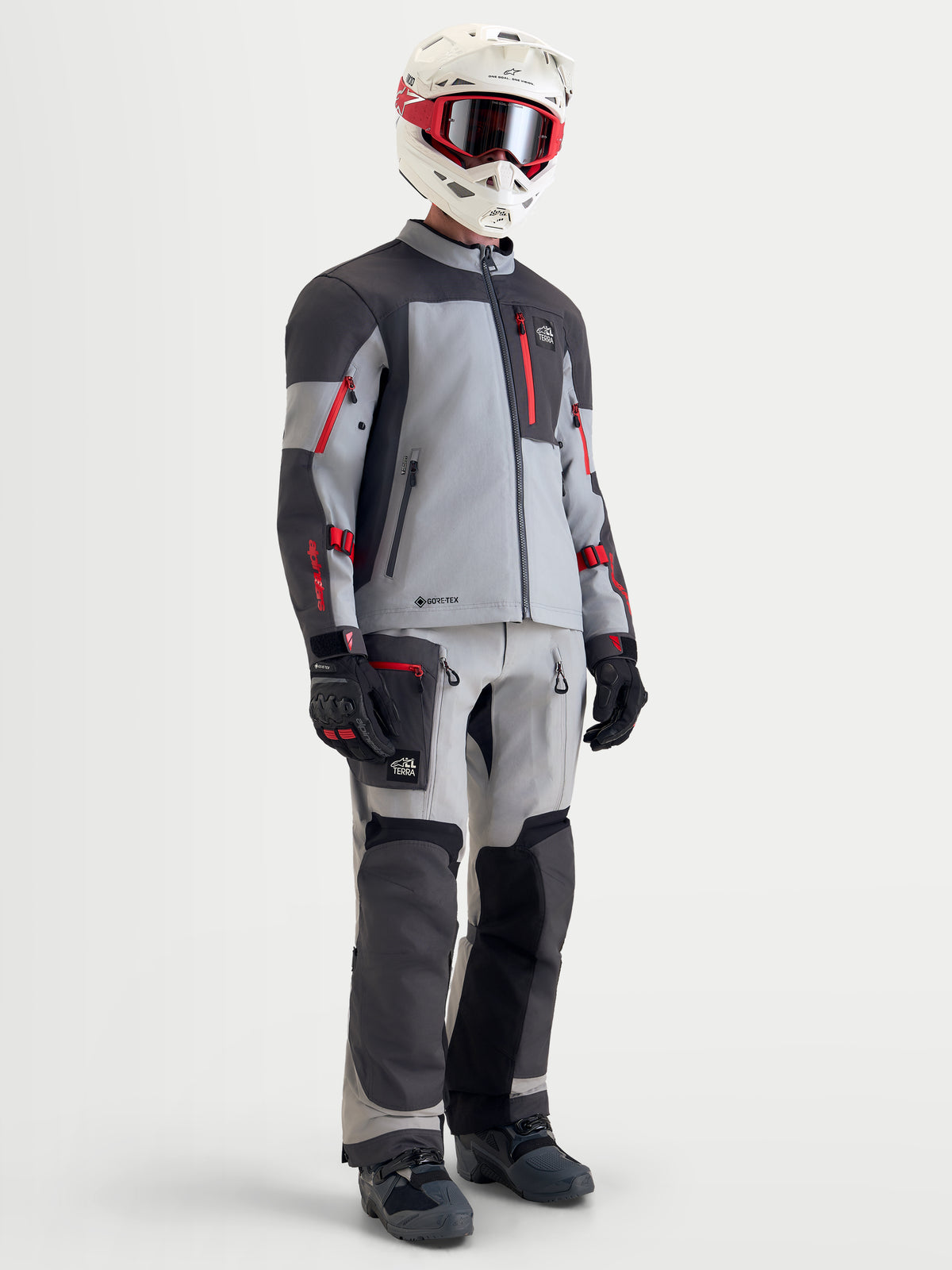 Alpinestars Arenis Gore-Tex Gear Set, Herren-Abenteuer-Motorradkombi in Grau, Dunkelgrau und Rot, Ganzkörperansicht an Model mit passendem Helm, Schutzbrille, Handschuhen und Stiefeln, wasserdichte Allterrain-Schutzausrüstung