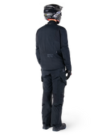 Rear view of a rider wearing the Alpinestars St-7 Prime GORE-TEX Jacket in black, paired with matching black touring pants, a black motorcycle helmet with white logo, and black riding boots, full protective adventure gear for touring and commuting.