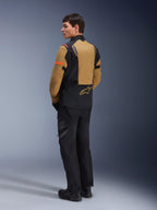 Alpinestars ST-7 2L GORE-TEX Jacke, Adventure-Motorradjacke, Gobi-Braun und Schwarz, Rückansicht eines Models in passender Fahrhose und Stiefeln, mit orangefarbenen Akzenten an den Ärmeln, wasserdichtem laminiertem Obermaterial und Alpinestars-Logo, entwickelt für Touren und Straßenfahrten