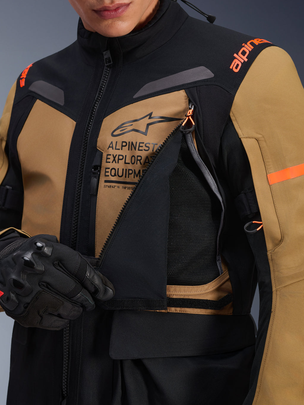 Alpinestars ST-7 2L GORE-TEX Jacke, Adventure-Touring-Motorradjacke, Gobi-Braun und Schwarz, Nahaufnahme des geöffneten Belüftungspanels an der Brust mit atmungsaktivem Mesh-Gewebe, Alpinestars Exploration Equipment Branding und orangefarbene Akzente.