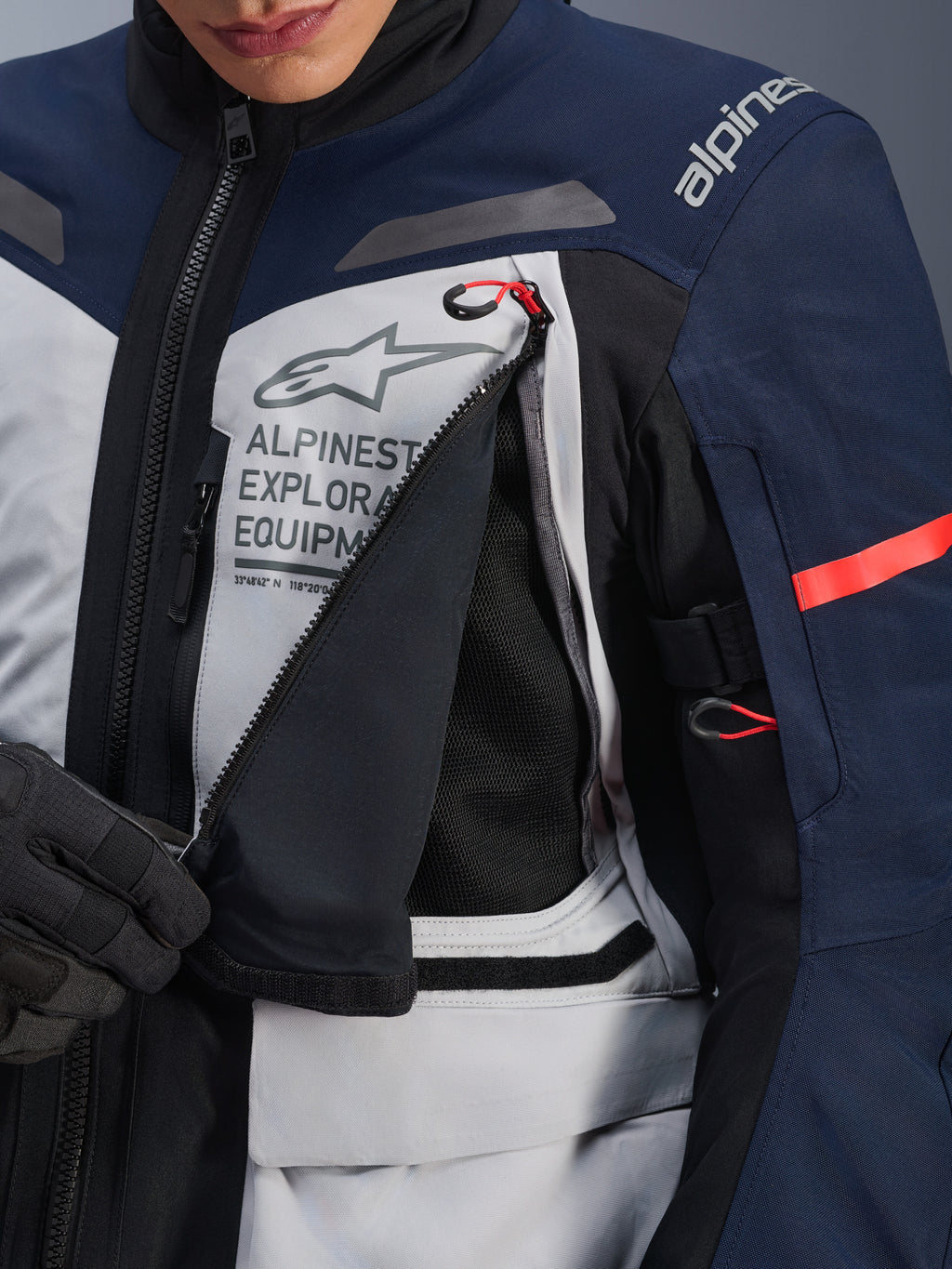 Alpinestars ST-7 2L GORE-TEX Jacke, Adventure-Tourenjacke, Ice Gray, Dunkelblau und Schwarz, Detailansicht des geöffneten Brust-Belüftungspanels mit schwarzem Mesh, Alpinestars Exploration Equipment Logo und roten Akzenten an den Zuglaschen