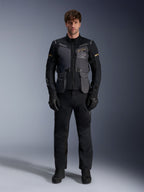 Männliches Model trägt die Alpinestars ST-7 2L GORE-TEX Jacke in Deep Gray Black Dark Khaki, mit dem „ALPINESTARS EXPLORATION EQUIPMENT“-Branding auf der Brust, kombiniert mit passender schwarzer Motorradhose, Handschuhen und Stiefeln, Studio-Frontansicht.