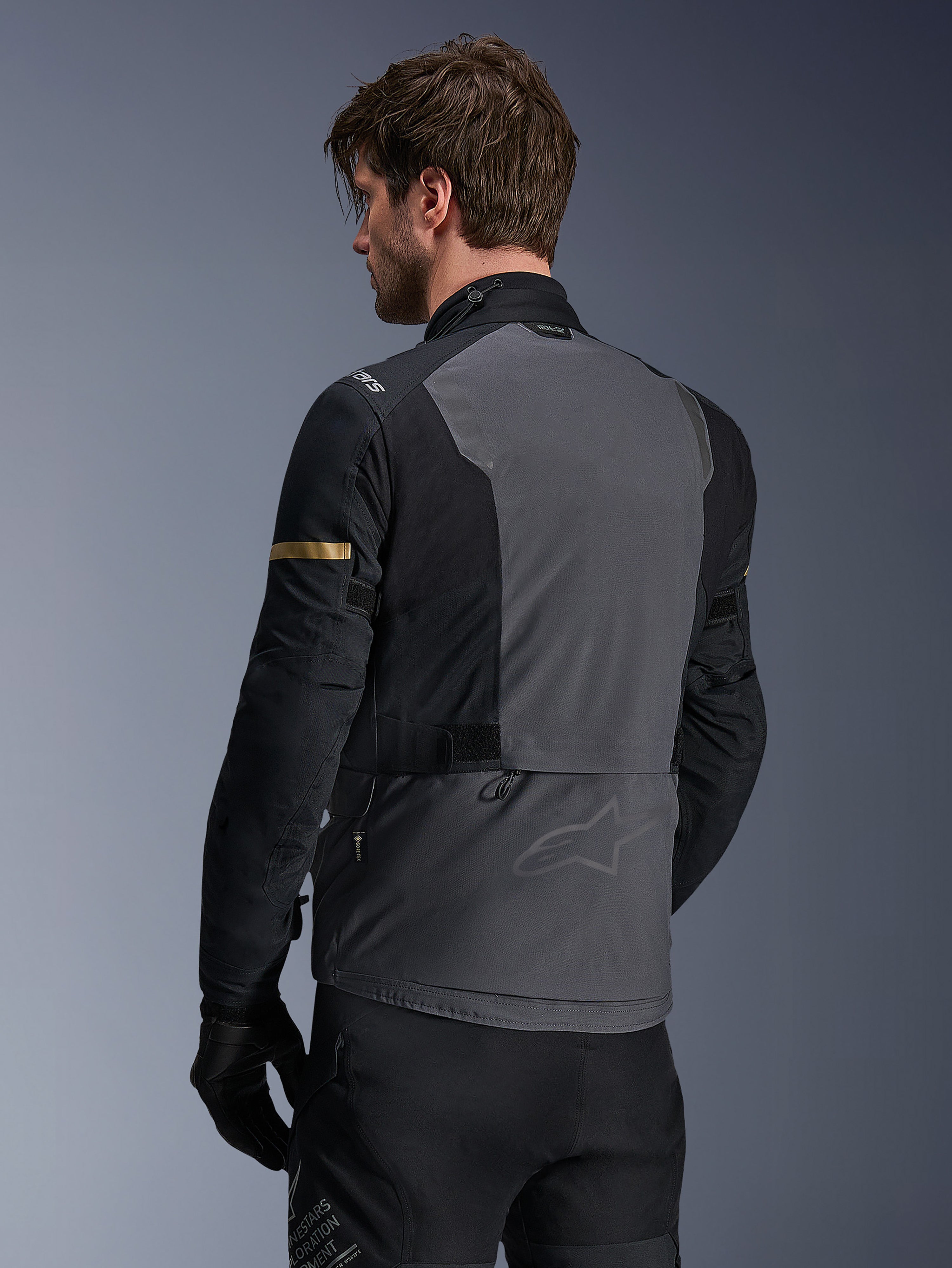 Alpinestars ST-7 2L GORE-TEX Jacke, Motorradjacke, Deep Gray Black und Dark Khaki, Rückansicht mit großem grauen Rückenelement und dezentem Branding, schwarze Ärmel mit goldfarbenen Khaki-Akzenten, abenteuerbereites wasserdichtes Textildesign