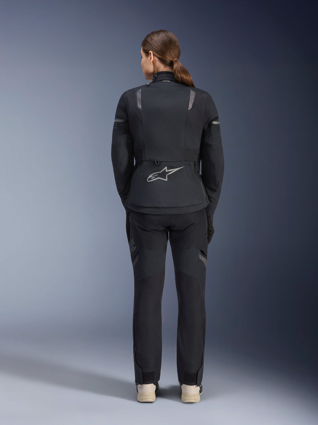 Alpinestars Damen Stella ST-7 2L GORE-TEX Jacke, Schwarz und Dunkelgrau, Rückansicht mit silbernem Alpinestars-Logo am unteren Rücken, kombiniert mit passender schwarzer Textilhose, Adventure-Touring-Motorradausrüstung