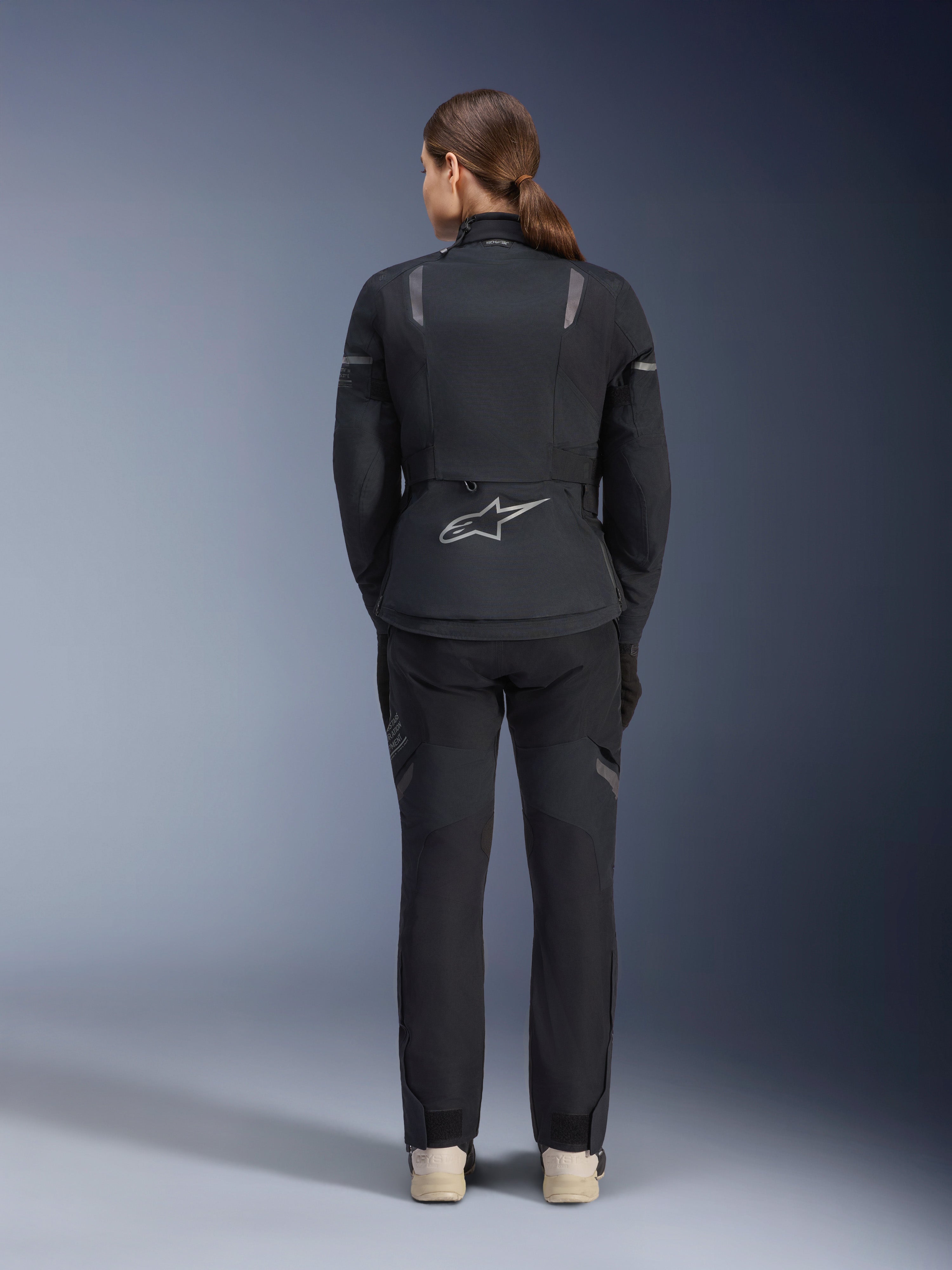 Alpinestars Damen Stella ST-7 2L GORE-TEX Jacke, Schwarz und Dunkelgrau, Rückansicht mit silbernem Alpinestars-Logo am unteren Rücken, kombiniert mit passender schwarzer Textilhose, Adventure-Touring-Motorradausrüstung