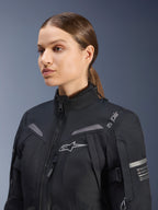 Alpinestars Stella ST-7 2L GORE-TEX Damenjacke, Schwarz, mit Brustlogo und technischen Koordinaten am Arm, wasserdichtes Textildesign mit hohem Kragen für Motorradtouring, Studio-Porträt einer Fahrerin