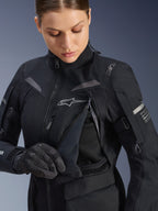 Alpinestars Damen Stella ST-7 2L GORE-TEX Jacke in Schwarz-Dunkelgrau, Detailansicht des geöffneten Brust-Belüftungspanels mit Mesh-Futter, Alpinestars-Logo und Schulter-Branding, konzipiert für Adventure-Road-Touring.