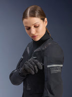 Alpinestars Stella ST-7 2L GORE-TEX Damenjacke, Adventure-Touring-Jacke, Schwarz und Dunkelgrau, getragen von einer Frau, die ein Ärmeldetail anpasst, mit reflektierenden Streifen und Koordinatengrafiken, strapazierfähiges Textil-Außenmaterial für Ganzjahresfahrten