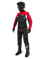 Alpinestars Pro-Dura Jacke, Offroad-Motorradjacke, Schwarz, Hellrot und Weiß, getragen mit kompletter Rennausrüstung inklusive schwarzem Helm mit roter Schutzbrille, schwarzer Hose und schwarz-weißen Stiefeln, strapazierfähiges Textil-Outfit für Enduro- und Trailfahrten