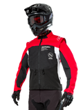Alpinestars Pro-Dura Jacke, Offroad-Enduro-Motorradjacke, Schwarz mit leuchtendem Rot und weißem Colorblocking, getragen von einem Fahrer mit schwarzem Helm und Brille, mit vorderen Reißverschlusstaschen und Alpinestars-Branding, strapazierfähige Textilkonstruktion für Trail-Fahrten