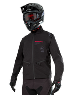 Alpinestars Lite-Dura Softshell Jacket, Black off-road motorcycle jacket with red branding and AS logo, worn with a black motocross helmet, red goggles, and black gloves, featuring zippered hand pockets and adjustable cuffs, designed for enduro riding.