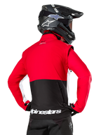 Alpinestars Lite-Dura Softshell-Jacke, Schwarz Hellrot Weiß, Rückansicht an einem Motocross-Fahrer, roter Oberkörper und Ärmel mit schwarzem Einsatz am unteren Rücken, Rückentasche mit Reißverschluss, weißes Alpinestars-Logo am Saum, getragen mit schwarzem Helm und Hose