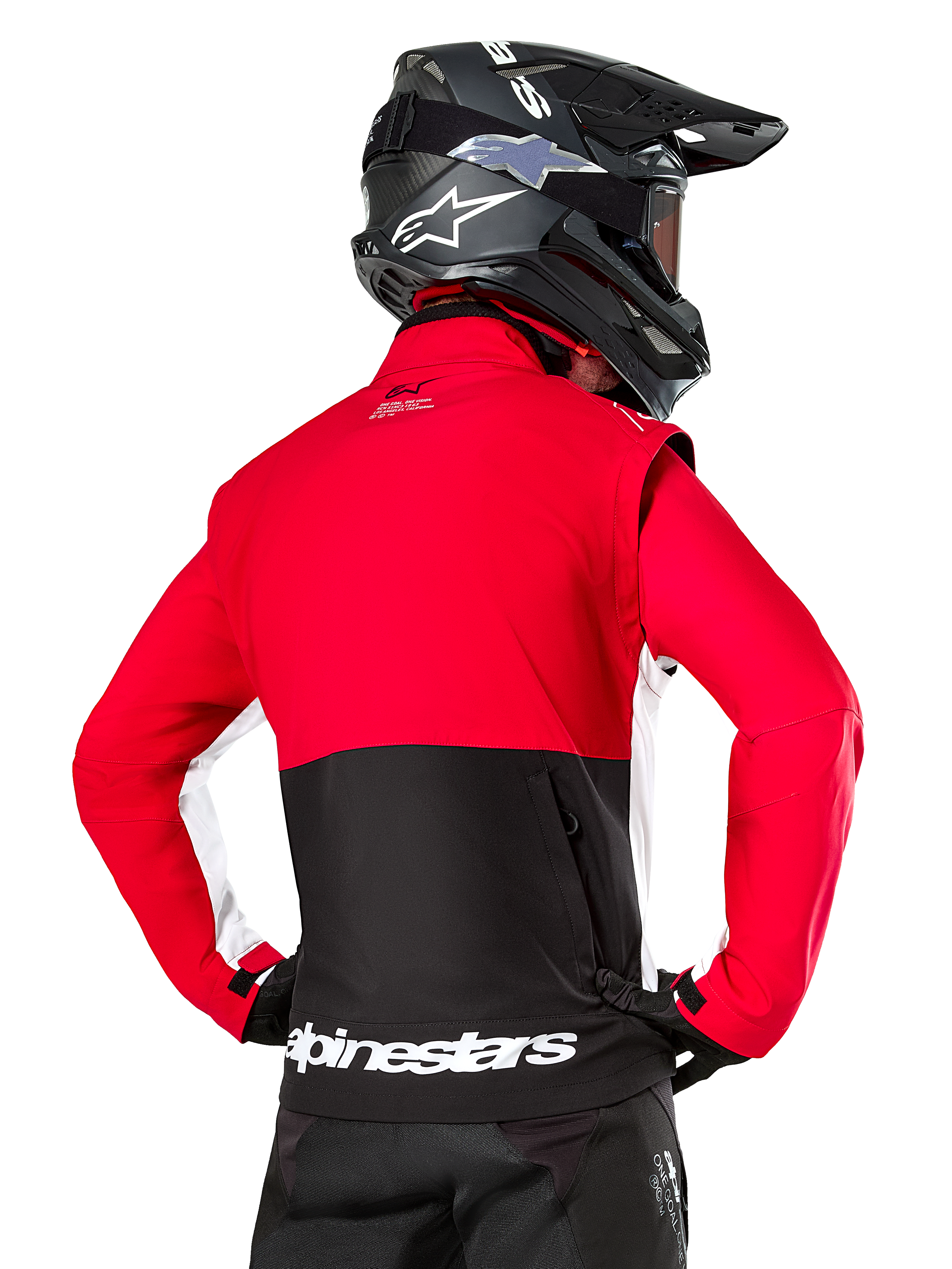 Alpinestars Lite-Dura Softshell-Jacke, Schwarz Hellrot Weiß, Rückansicht an einem Motocross-Fahrer, roter Oberkörper und Ärmel mit schwarzem Einsatz am unteren Rücken, Rückentasche mit Reißverschluss, weißes Alpinestars-Logo am Saum, getragen mit schwarzem Helm und Hose