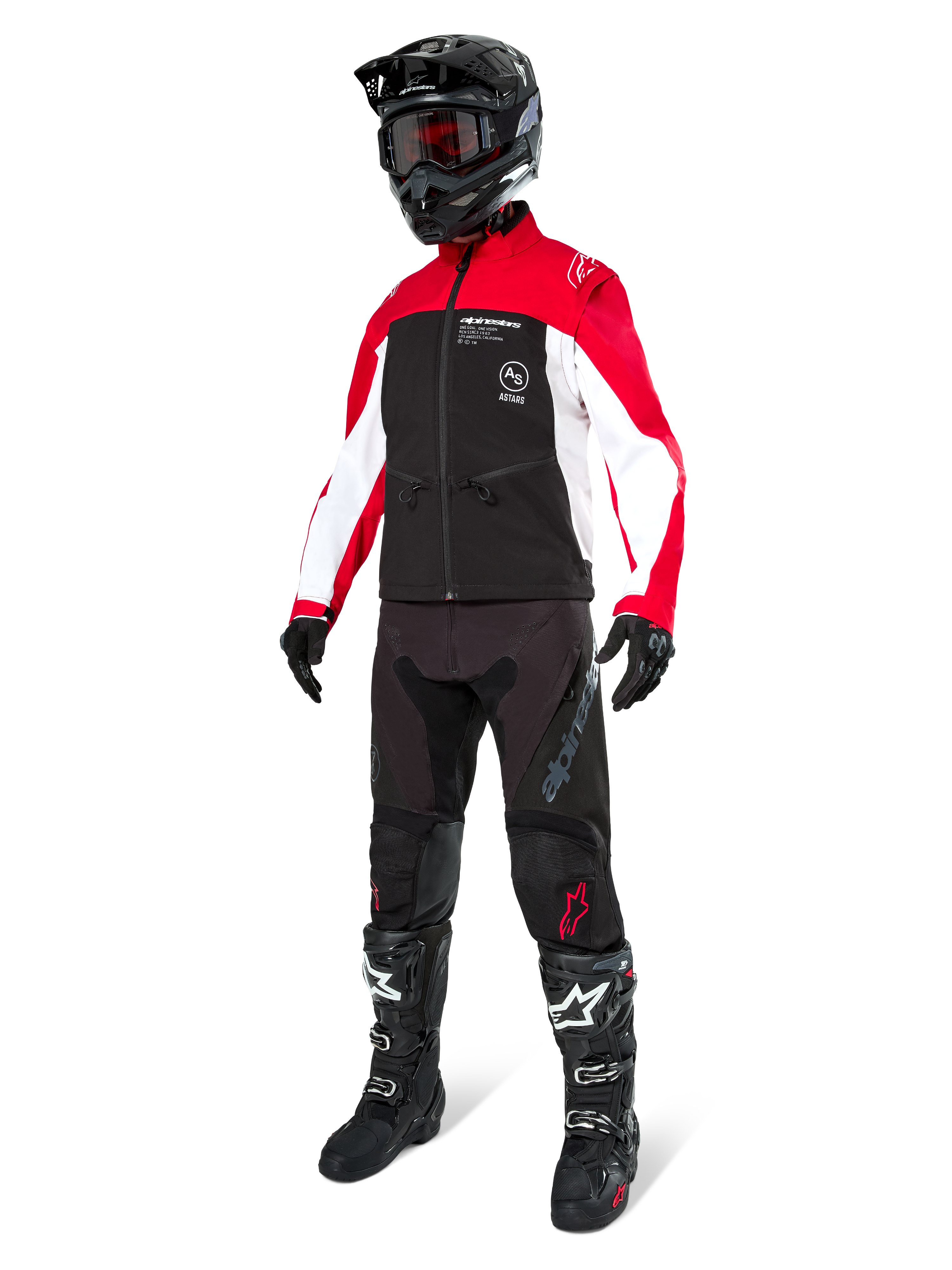 Motocross-Fahrer in der Alpinestars Lite-Dura Softshell-Jacke in Schwarz, leuchtendem Rot und Weiß, schwarzer Rumpf und rot-weiße Ärmel, kombiniert mit schwarzer Hose, schwarzem Helm mit roter Brille und schwarz-weißen Stiefeln, komplette Offroad-Rennausrüstung.