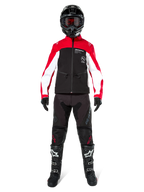 Motocross-Fahrer in der Alpinestars Lite-Dura Softshell-Jacke in Schwarz, Bright Red und Weiß, kombiniert mit einer schwarzen Offroad-Hose, schwarz-weißen Stiefeln und einem schwarzen Helm mit Goggles, komplette Ausrüstung für Enduro-Rennen