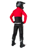 Motocross-Fahrer von hinten in der Alpinestars Lite-Dura Softshell-Jacke, Schwarz, Bright Red und Weiß, mit rotem oberen Panel und schwarzem unteren Bereich mit weißem Branding, kombiniert mit schwarzer Hose, schwarzem Helm und schwarzen Stiefeln, abgestimmtes Enduro-Outfit für Geländefahrten