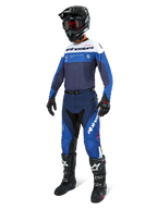 Motocross rider wearing Alpinestars Pro-Dura Pants in Navy, Bright Blue, and White, paired with a matching long-sleeve jersey, black helmet with red goggles, black gloves, and black and white boots, coordinated outfit for enduro and off-road racing.