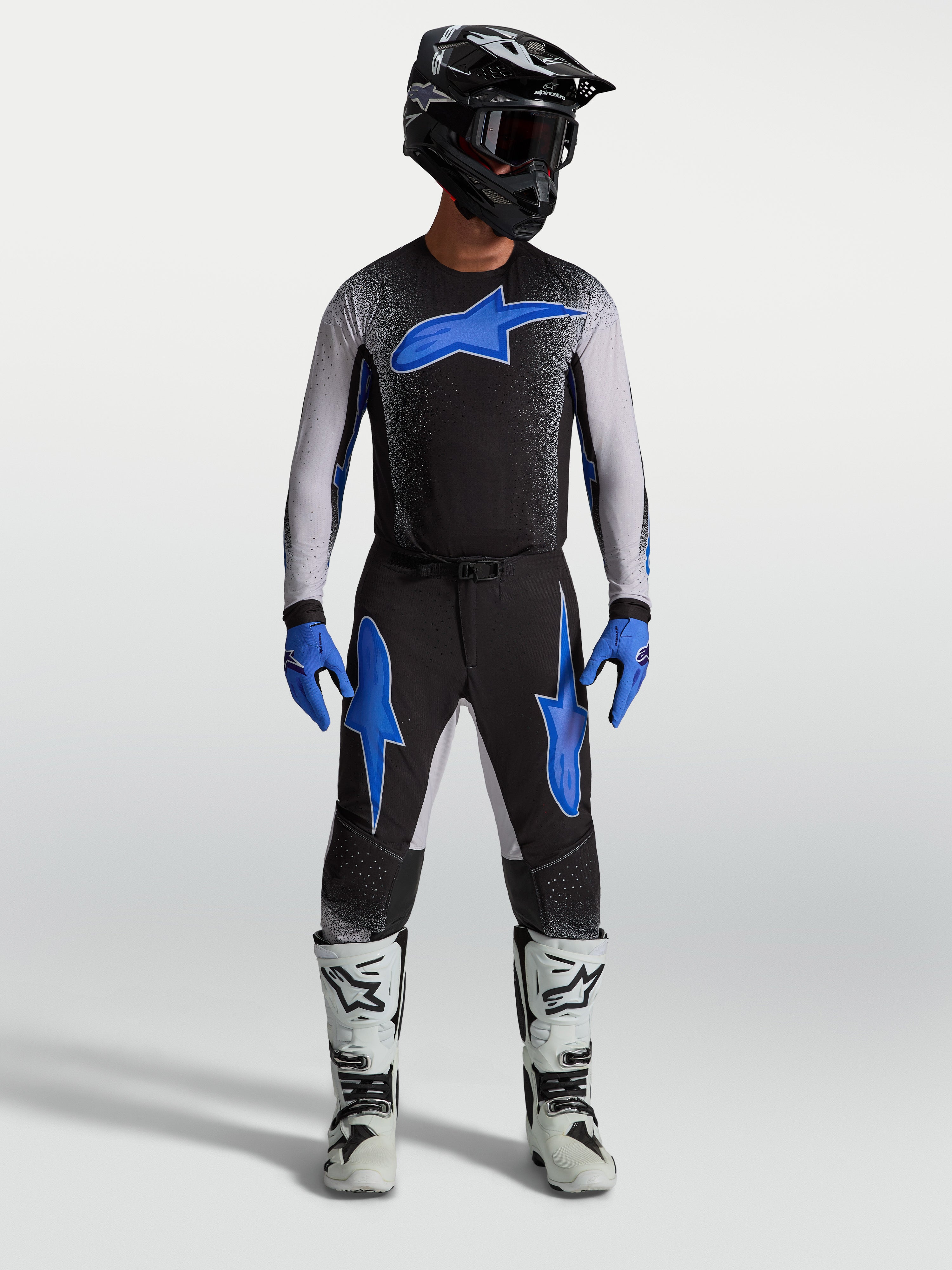 Alpinestars Supertech Hiten AFD Hose, Motocross-Hose für Herren, Schwarz und Blau, am Model mit passendem Trikot und weißen Motorradstiefeln, professionelle Offroad-Rennsport-Ausrüstung