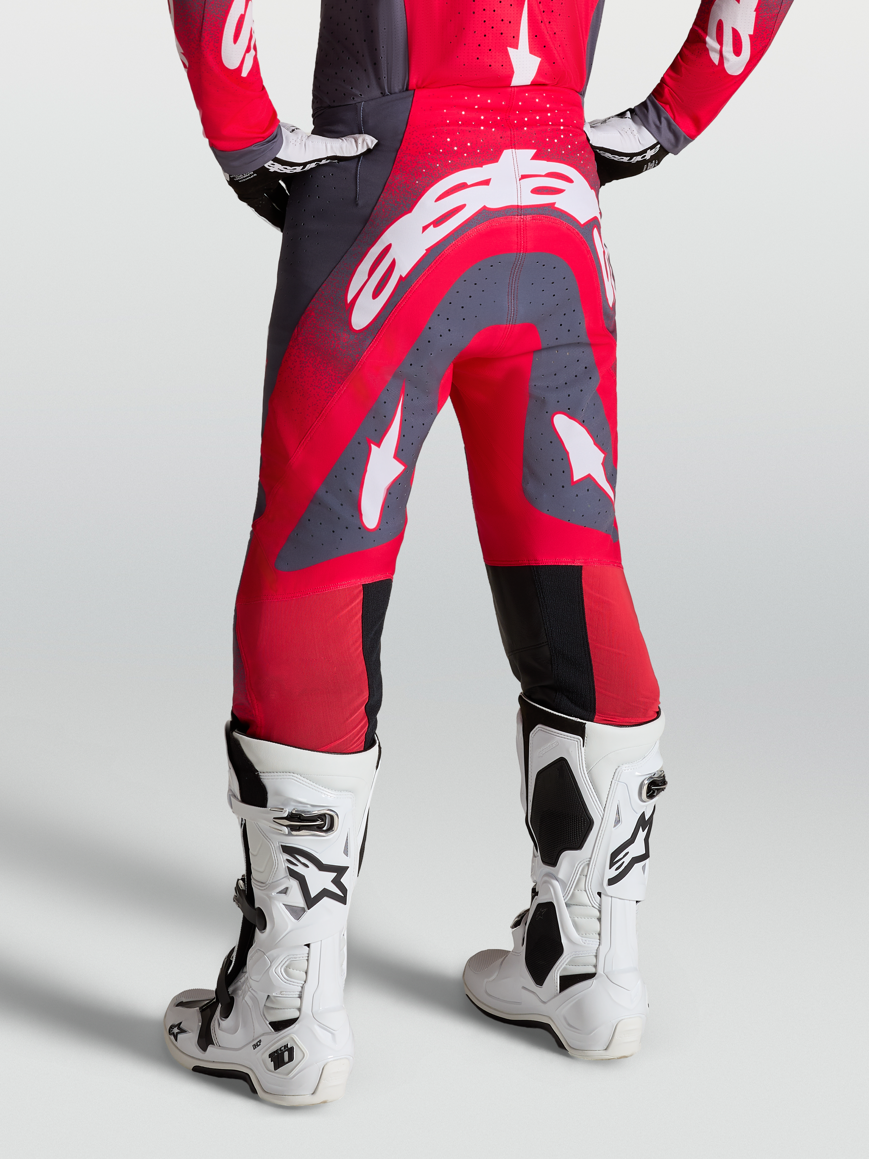 Alpinestars Supertech Hiten AFD Hose, Motocross-Hose in Rot und Grau, Rückansicht am Model mit weißen Rennstiefeln.