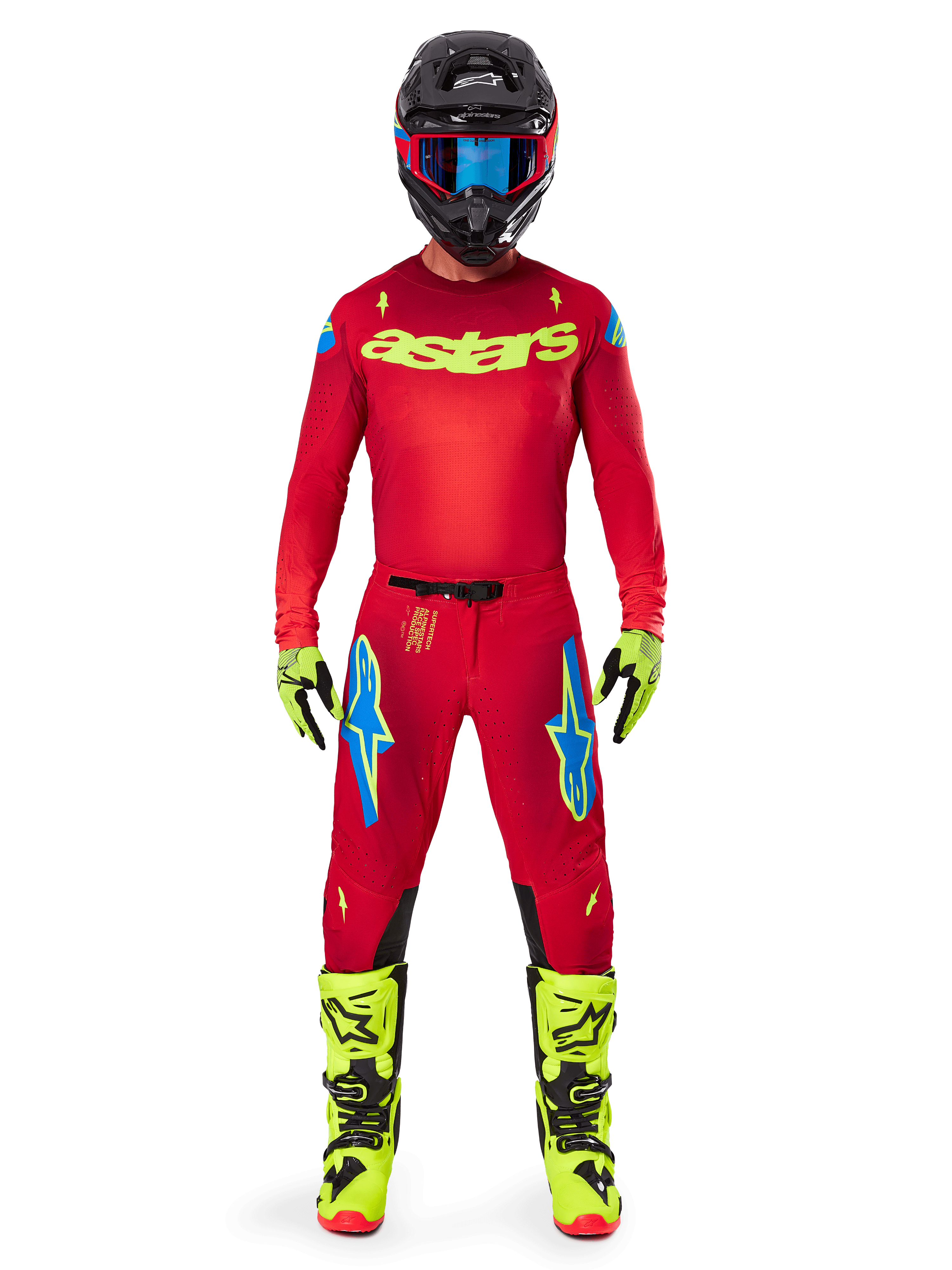 Motocross-Fahrer in kompletter Rennausrüstung, rotes Trikot mit gelbem Fluo-Astars-Logo, Alpinestars 2025 Supertech Maker Hose in Bright Red und Yellow Fluo, mit blauen Logos an den Oberschenkeln, gelbe Fluo-Handschuhe und -Stiefel, schwarzer Helm mit blauer Brille, koordiniertes Motocross-Outfit auf Profi-Niveau