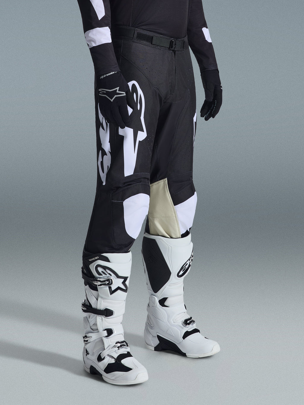 Alpinestars 2026 Racer Air Riway Hose, Motocross-Hose, Schwarz und Weiß, getragen mit weiß-schwarzen Tech Series Stiefeln und schwarzem Langarmtrikot, mit weißem Alpinestars-Branding, lasergeschnittenen Perforationen und hellbraunen Knie-Einsätzen aus Ziegenleder für Offroad-Performance.