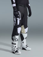 Alpinestars 2026 Racer Air Riway Hose, Motocross-Hose, Schwarz und Weiß, getragen mit weiß-schwarzen Tech Series Stiefeln und schwarzem Langarmtrikot, mit weißem Alpinestars-Branding, lasergeschnittenen Perforationen und hellbraunen Knie-Einsätzen aus Ziegenleder für Offroad-Performance.