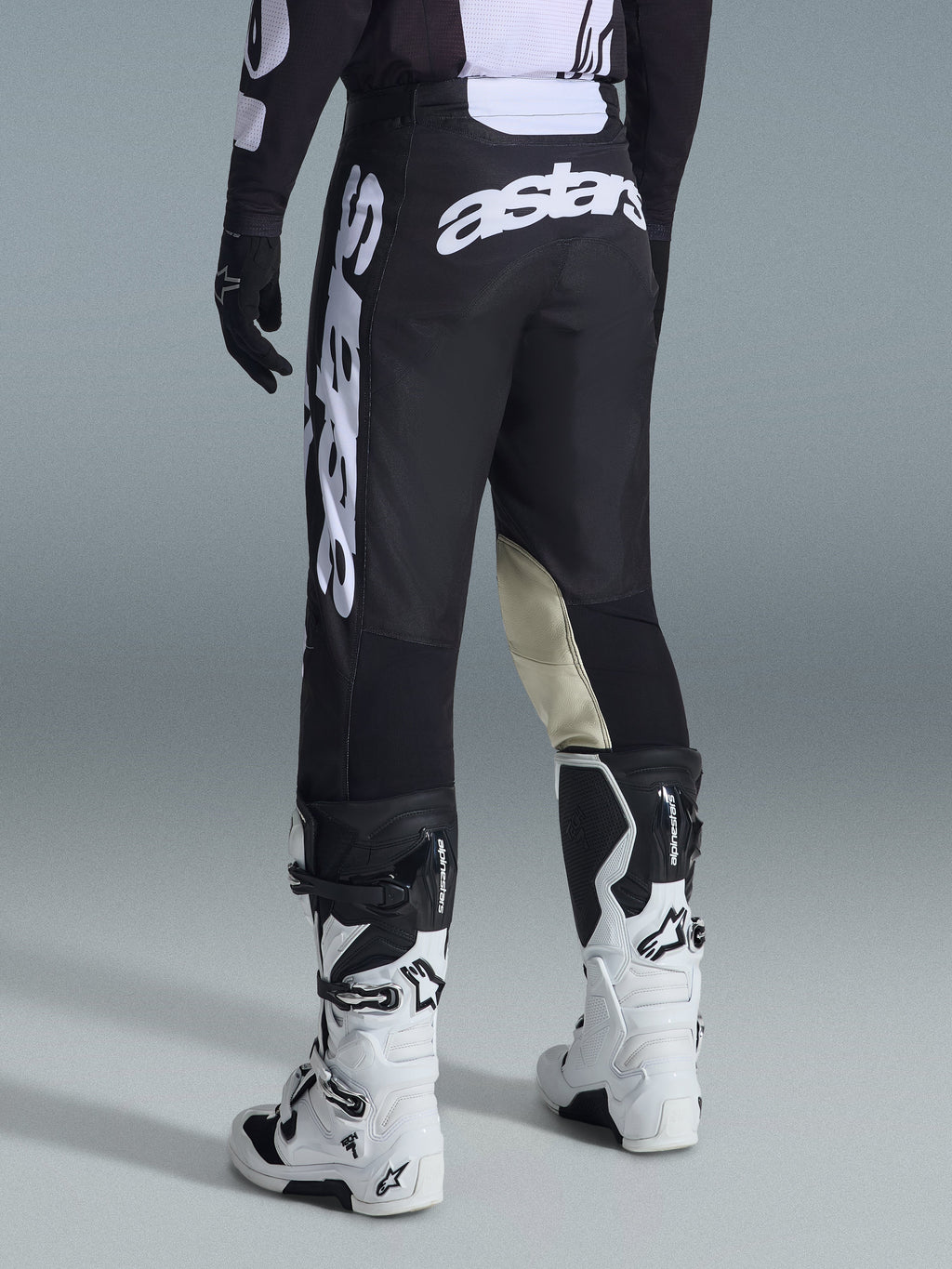 Alpinestars 2026 Racer Air Riway Hose, Motocross-Hose, Schwarz und Weiß, Rückansicht mit großem weißem Astars-Branding auf dem Gesäß und den Beinen, beigefarbene Leder-Einsätze an den Knieinnenseiten, getragen mit weiß-schwarzen Tech 7 Stiefeln, hochwertige Offroad-Rennbekleidung.