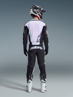 Motocross-Fahrer in der Rückansicht mit Alpinestars 2026 Racer Air Riway Hose in Schwarz und Weiß, passendem schwarz-weißem Langarm-Trikot, weiß-schwarzen Rennstiefeln und schwarzem Helm mit Alpinestars-Branding.