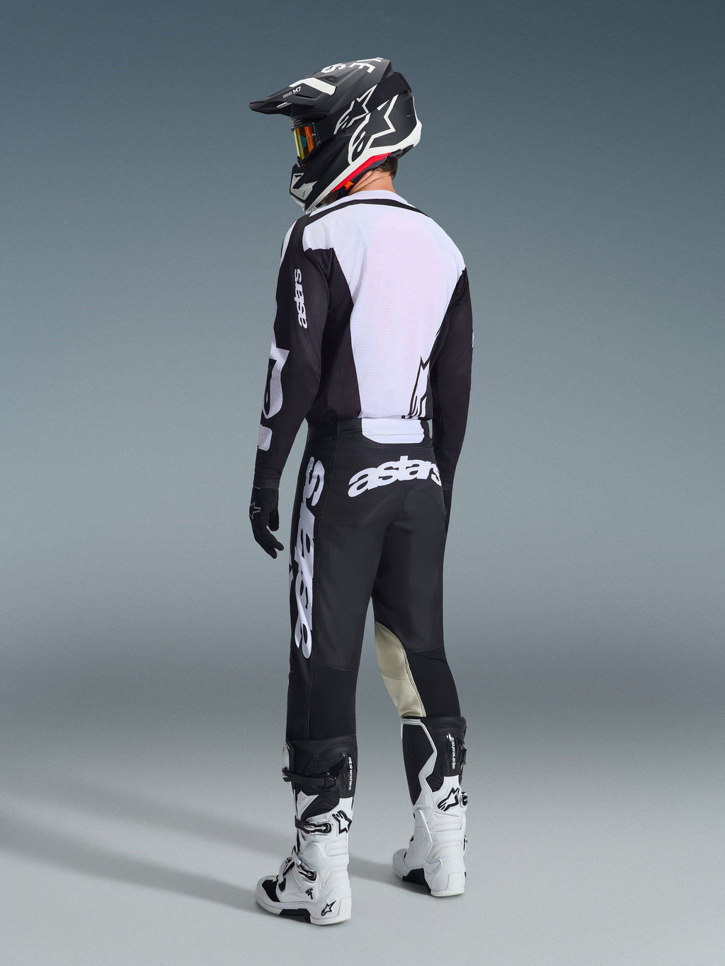Motocross-Fahrer in der Rückansicht, trägt die Alpinestars 2026 Racer Air Riway Hose in Schwarz und Weiß, kombiniert mit einem passenden belüfteten Trikot, einem schwarz-weißen Helm und weißen Motocross-Stiefeln, mit markantem weißen 'astars'-Branding auf dem Gesäß.
