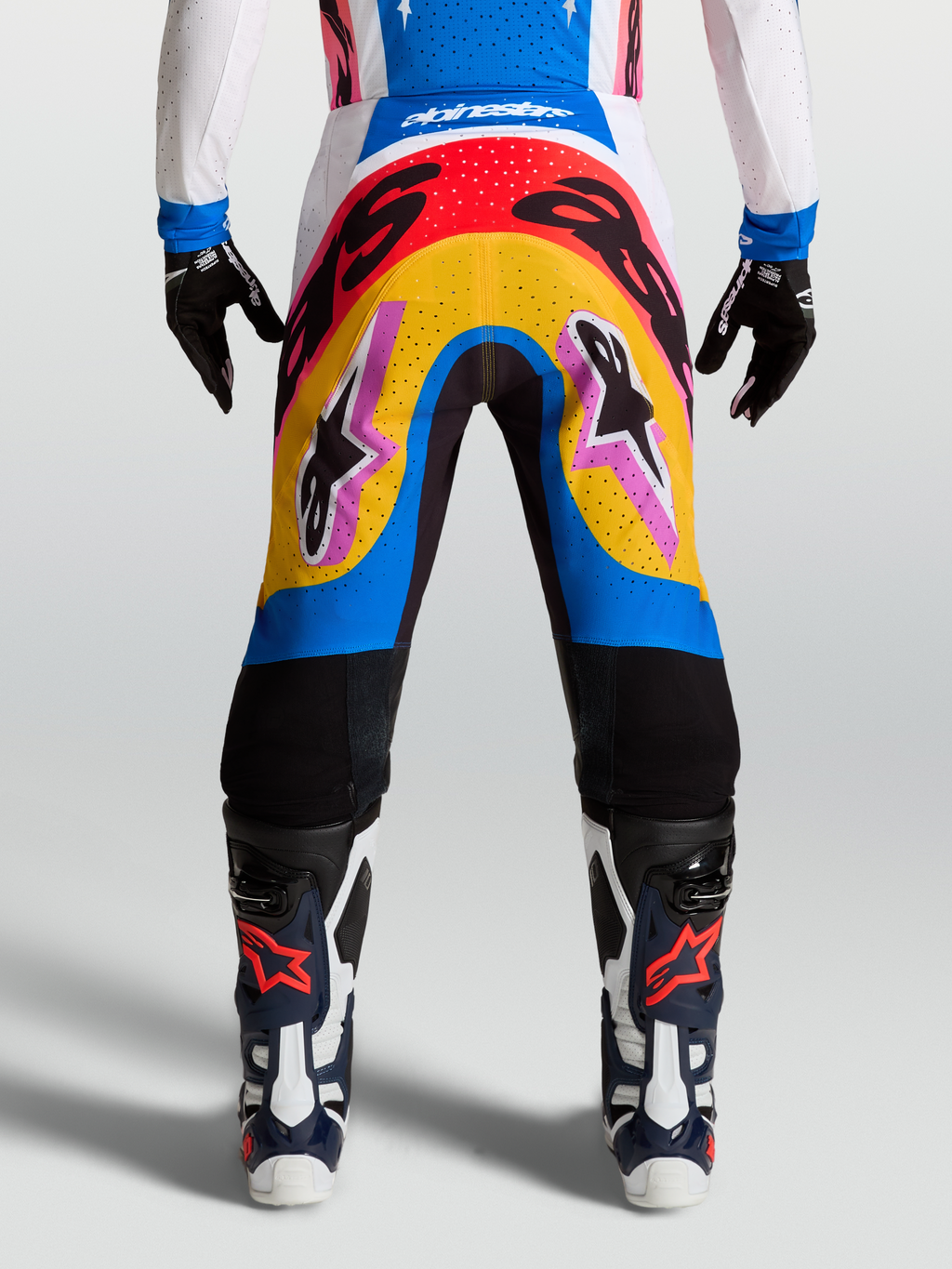 Alpinestars Supertech Dyna Hosen, Motocross-Rennsport-Hose, modernes mehrfarbiges Design in Blau und Gelb, leichtes Stretch-Ripstop-Material getragen von einem Model mit Handschuhen und Stiefeln.