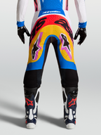 Alpinestars Supertech Dyna Hosen, Motocross-Rennsport-Hose, modernes mehrfarbiges Design in Blau und Gelb, leichtes Stretch-Ripstop-Material getragen von einem Model mit Handschuhen und Stiefeln.