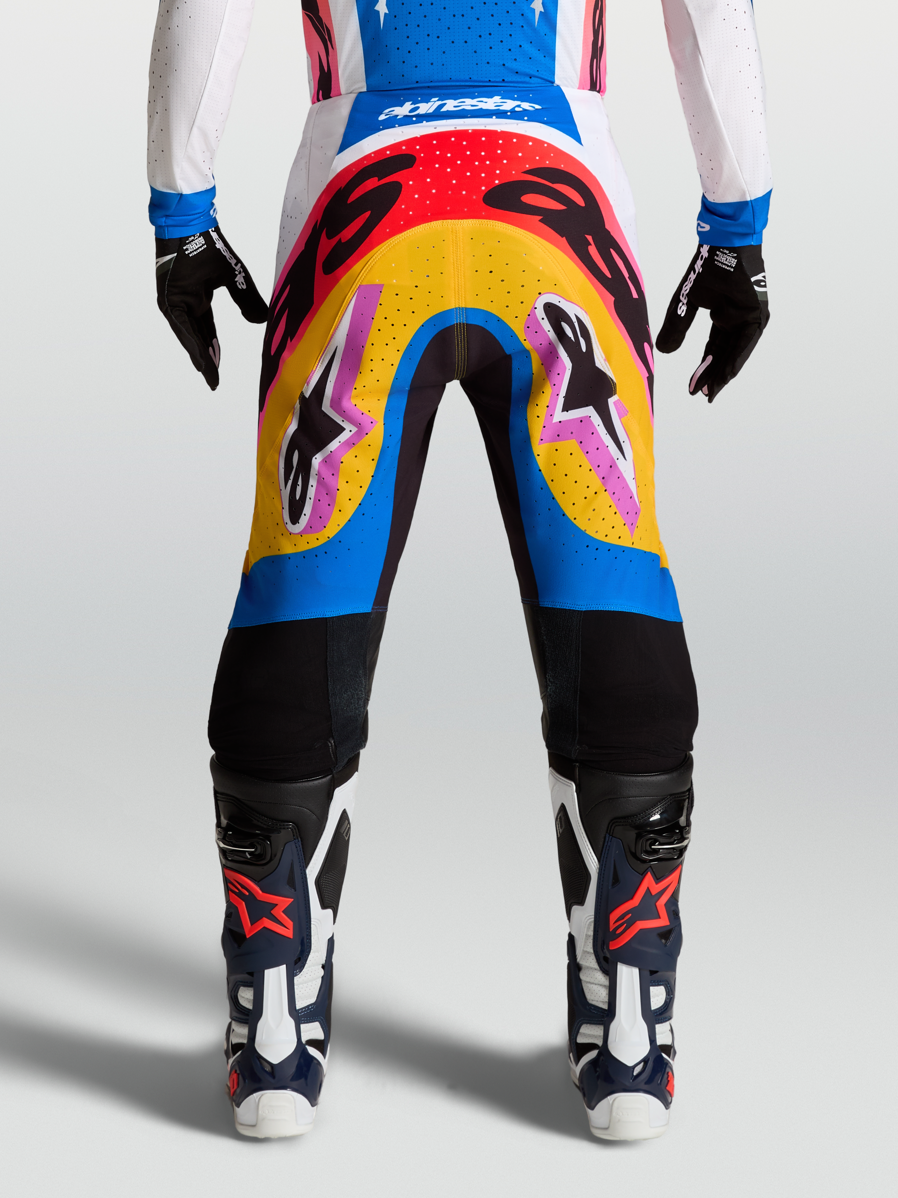 Alpinestars Supertech Dyna Hosen, Motocross-Rennsport-Hose, modernes mehrfarbiges Design in Blau und Gelb, leichtes Stretch-Ripstop-Material getragen von einem Model mit Handschuhen und Stiefeln.
