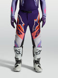 Alpinestars Supertech Dyna Hose, Motocrosshose für Herren, Lila und Pink Fluo mit orangen Details, athletische Rennpassform aus Stretch-Ripstop, getragen mit weißen Stiefeln für den Offroad-Einsatz.