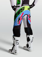 Alpinestars Supertech Dyna Hose, Motocross-Rennsport-Hose für Herren, Flieder, Grün und Schwarz, Rückansicht mit perforiertem Stretch-Ripstop-Gewebe und Ziegenleder-Kniepanels, getragen mit weißen Tech 10 Stiefeln.