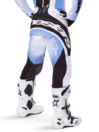 Alpinestars 2025 Techstar Melt Hose, Motocross-Hose, Schwarz, Blau und Weiß, Rückansicht mit markantem Alpinestars-Schriftzug am Gesäß und Stern-Logos auf den Beinen, kombiniert mit weiß-schwarzen Tech 10 Stiefeln, professionelle Offroad-Rennausrüstung