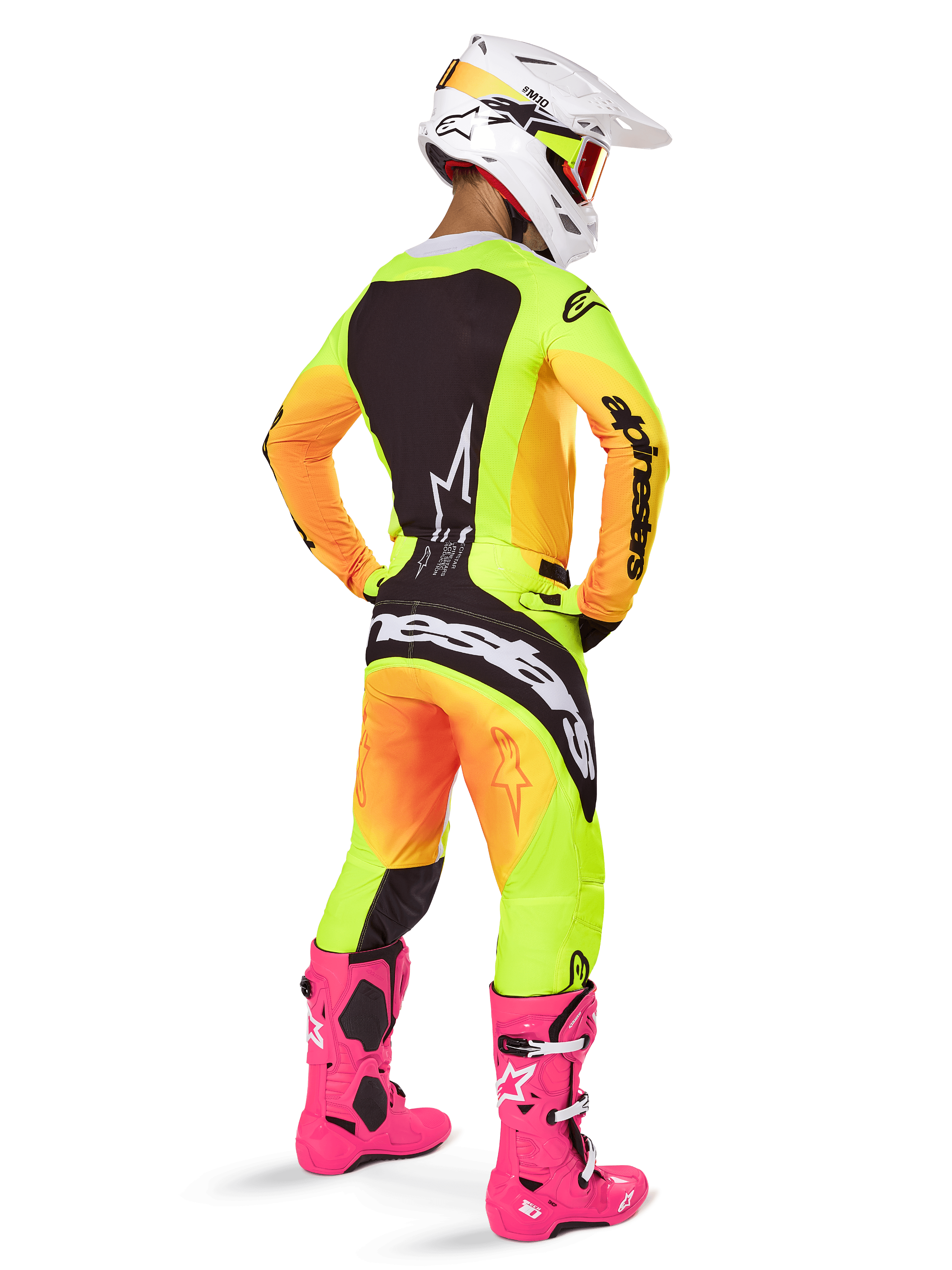 Motocross rider from behind wearing the Alpinestars 2025 Techstar Melt Gear Set, yellow and orange gradient jersey and pants with black panels, white helmet with red goggles, bright pink boots, coordinated racing outfit for off-road performance