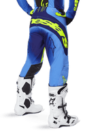 Alpinestars 2025 Techstar Melt Hose, Motocross-Hose, Blau und Gelb Fluo, Rückansicht mit großem gelbem Branding auf dem Gesäß und den Oberschenkeln, getragen mit weißen Motocross-Stiefeln und passendem blauem Trikot, athletische Rennpassform für Offroad-Fahrten