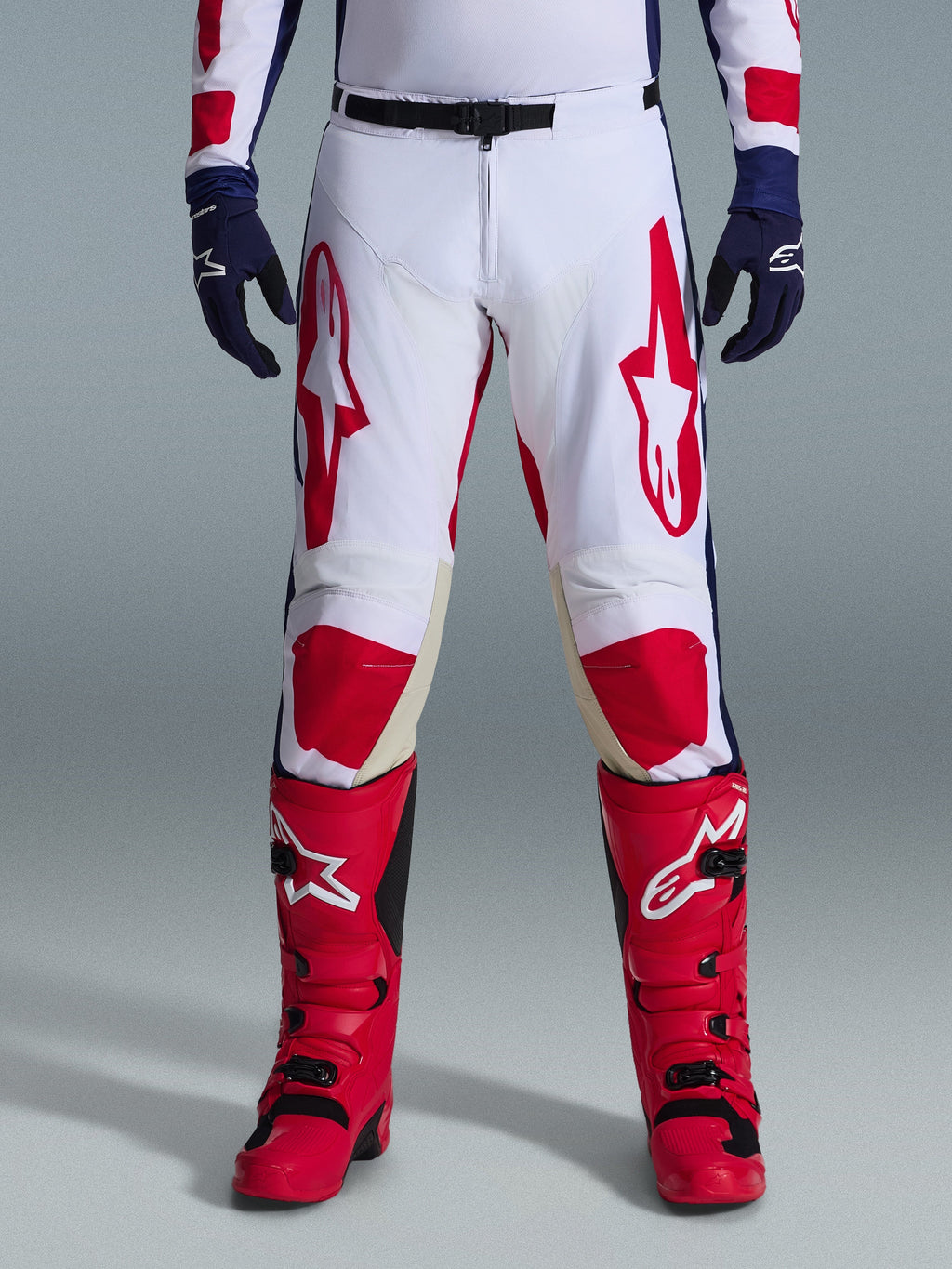 Alpinestars 2026 Racer Riway Hose, Motocross-Hose, Wei&szlig;, Blau und Rot, getragen mit roten Stiefeln und dunkelblauen Handschuhen, mit gro&szlig;en roten Logos auf den Oberschenkeln und roten Knieeins&auml;tzen, sportliches, vorgeformtes Design mit verstellbarer Taillenschnalle