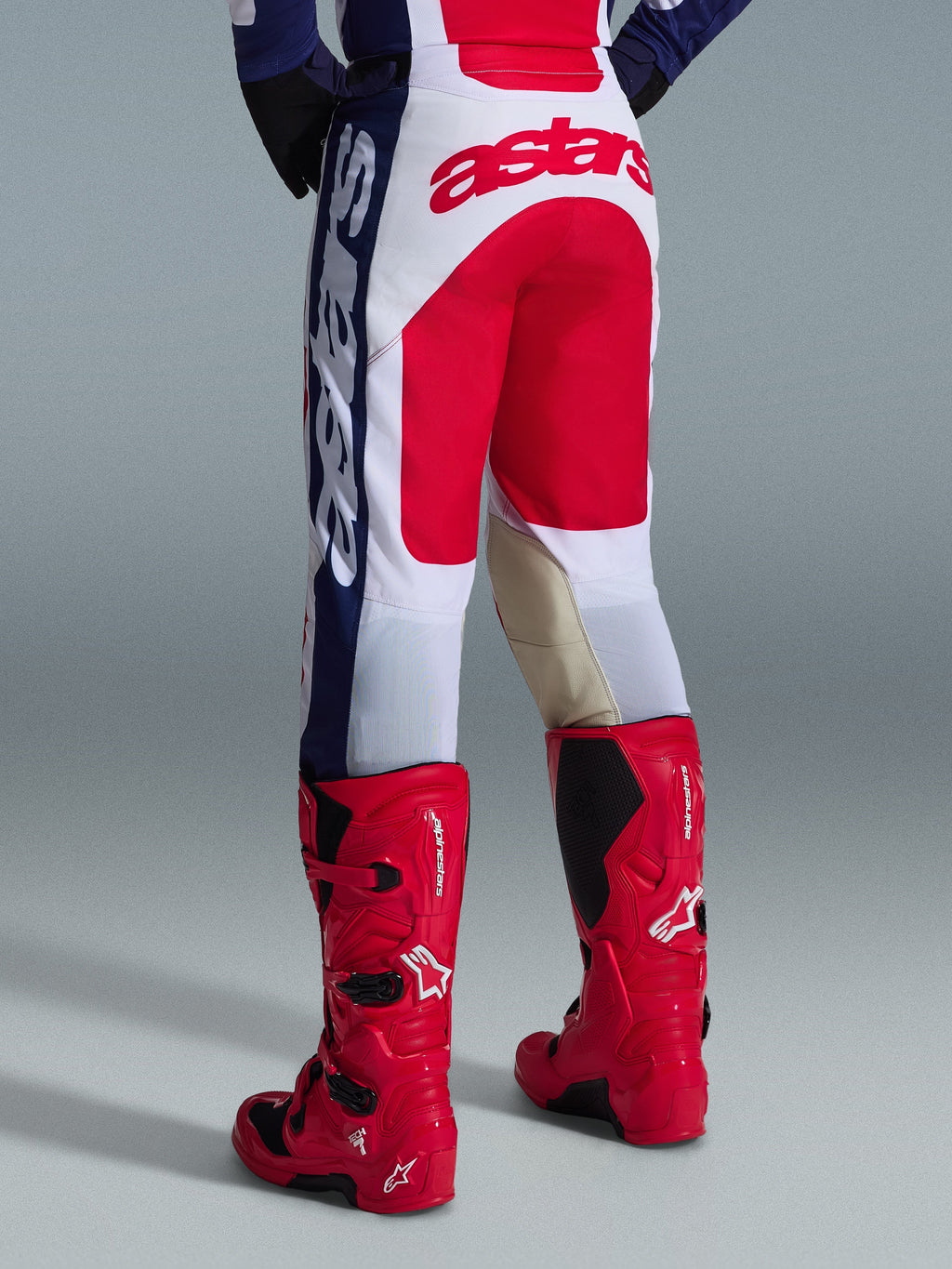 Alpinestars 2026 Racer Riway Hose, Motocross-Hose, Weiß, Blau und Rot, Rückansicht mit großem rotem Astars-Logo auf der Sitzfläche und beigen Leder-Innenknieeinsätzen, getragen mit roten Alpinestars Motocross-Stiefeln, Performance-Ausrüstung für den Offroad-Rennsport