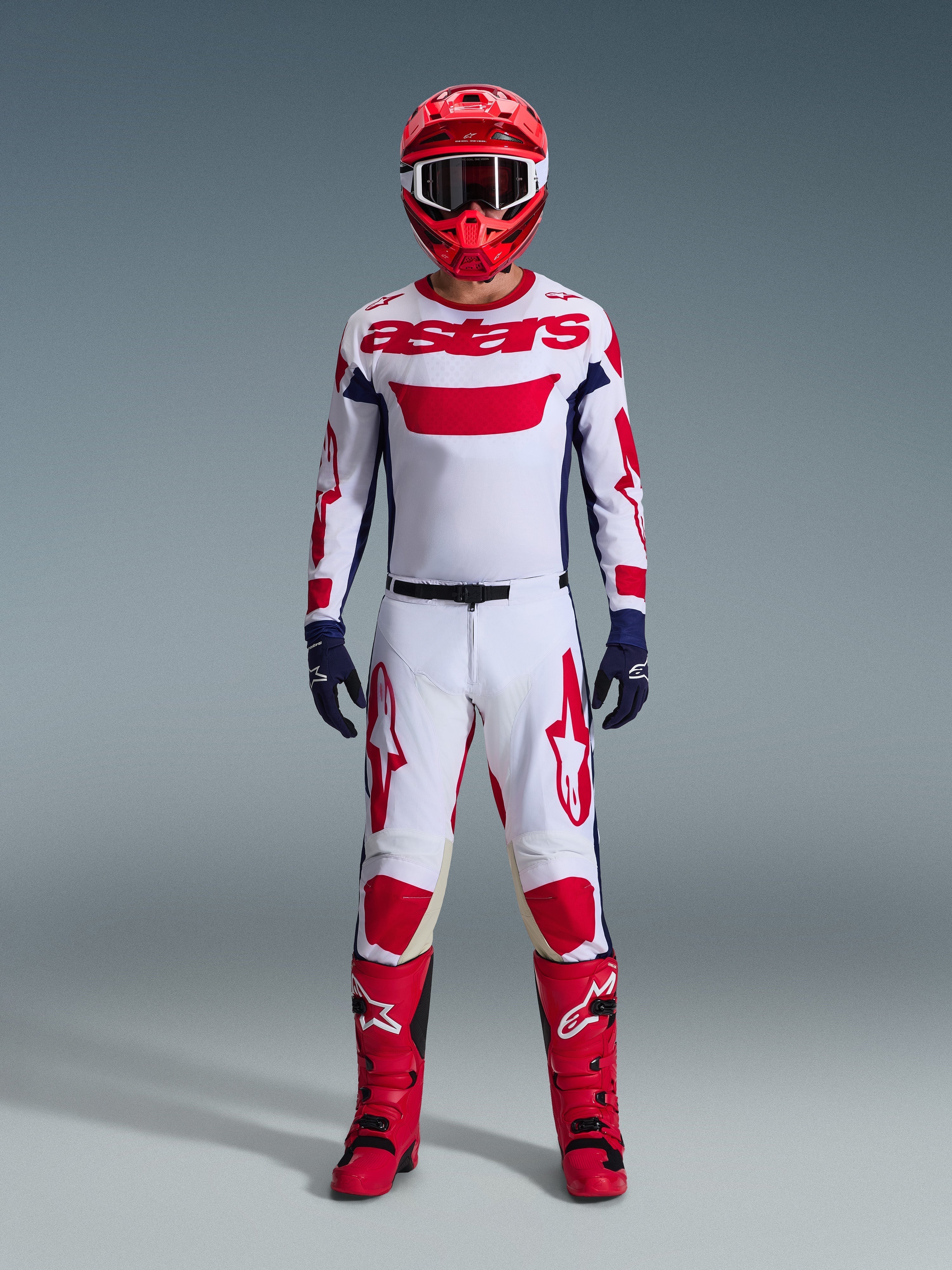 Motocross-Fahrer im Alpinestars 2026 Racer Riway Gear Set, weißes Trikot mit rotem „astars“-Branding und blauen Seiteneinsätzen, weiße Hose mit roten Grafiken, roter Helm und rote Stiefel, dunkelblaue Handschuhe, komplettes abgestimmtes Motocross-Outfit