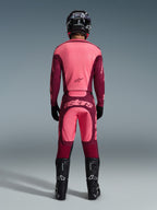 Rear view of a motocross rider wearing the 2026 Racer Riway Gear Set, pink and burgundy jersey, matching burgundy pants with light pink 'astars' logo on the seat, black helmet, black boots, and black gloves, coordinated outfit for off-road performance