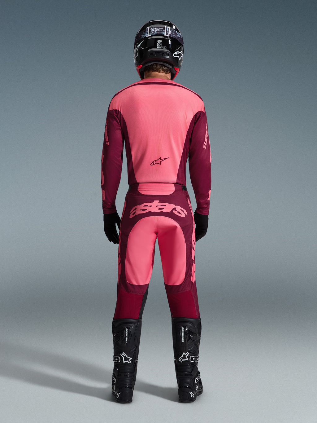 Motocross rider from the back wearing the Alpinestars 2026 Racer Riway Jersey and matching pants in Dark Red Coral, featuring black boots, a black helmet, and black gloves, coordinated high-performance gear for off-road racing