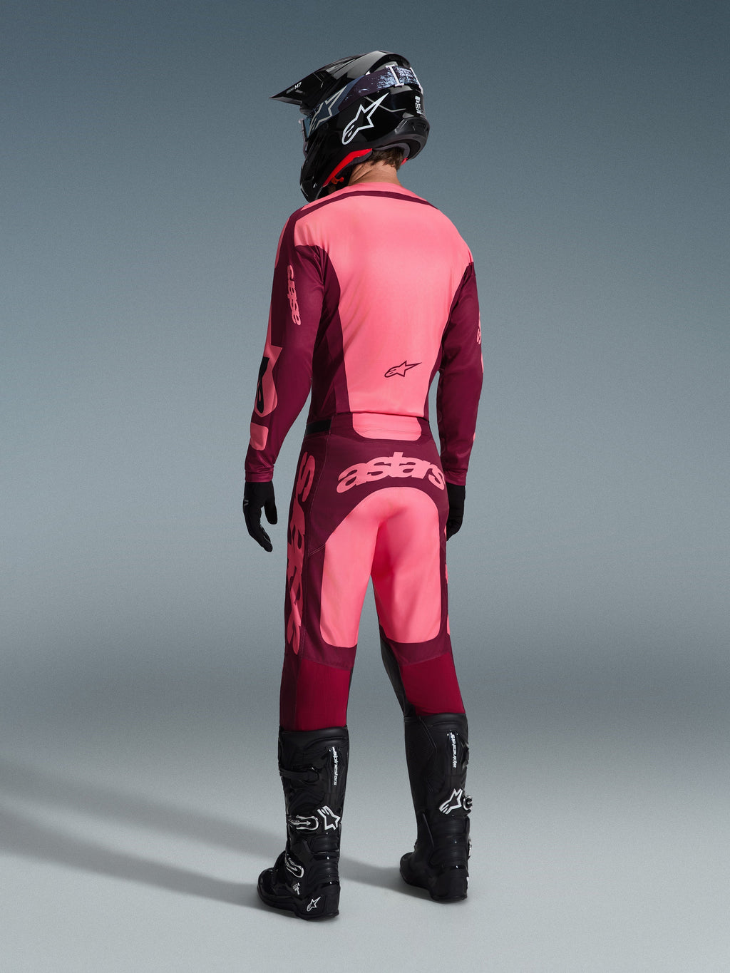 Alpinestars 2026 Racer Riway Pants, Motocross Pants, Dark Red Coral, rear view of a rider wearing a matching jersey, black helmet, and black boots, featuring bold coral branding on the seat and ergonomic athletic fit for off-road racing
