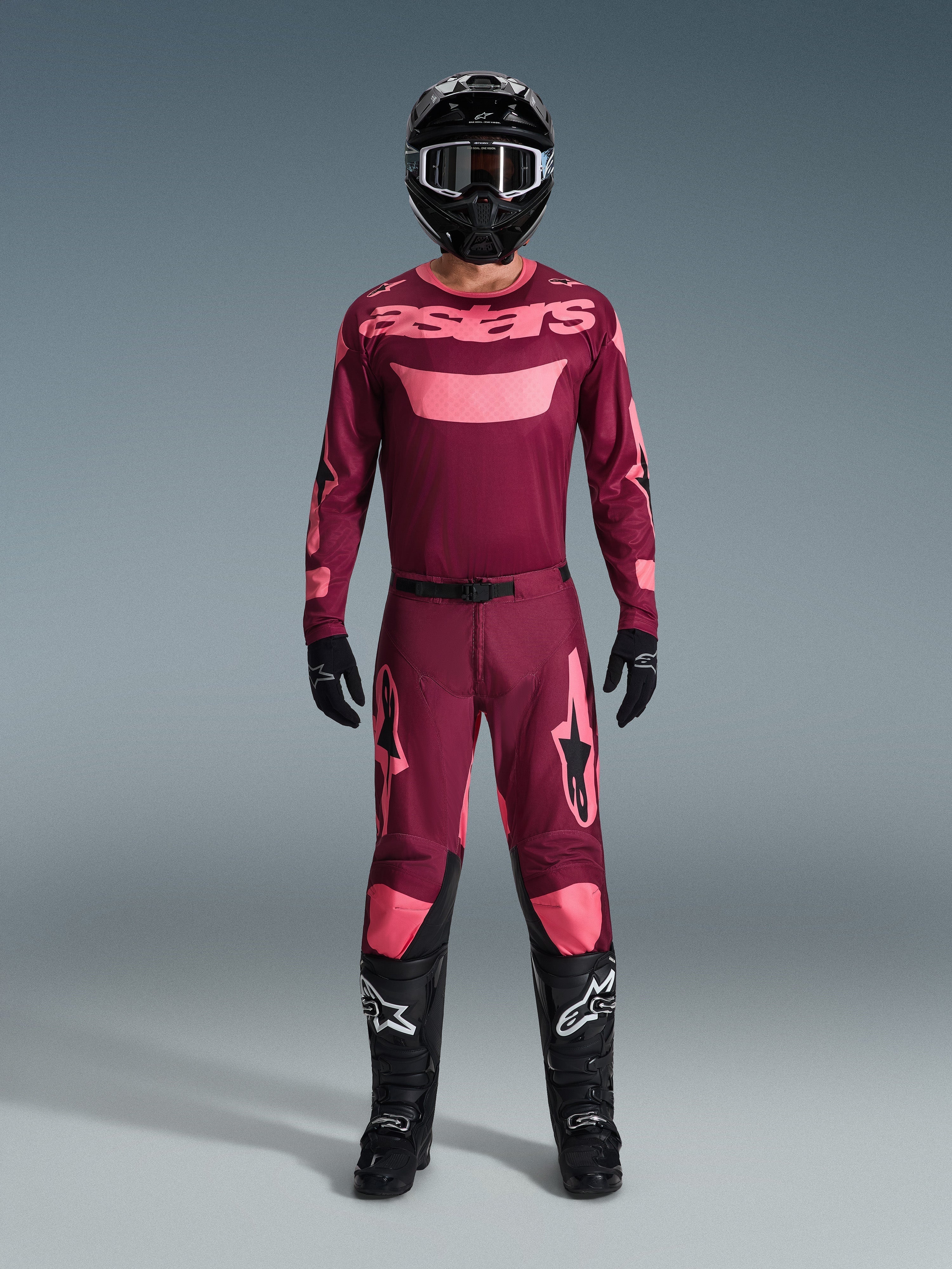Motocross rider wearing complete racing gear, 2026 Racer Riway Jersey in Dark Red Coral, matching dark red pants with coral accents, black helmet with white accents, black boots with white logos, and black gloves, coordinated outfit for off-road racing